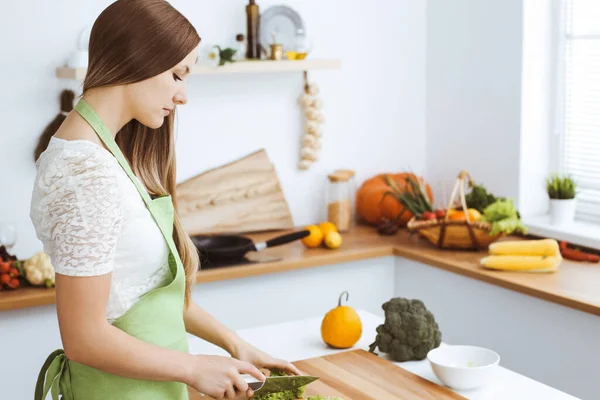 Mulher bonita vestida de avental está cozinhando refeição na cozinha. dona de casa cortando salada vegan fresco — Fotografia de Stock
