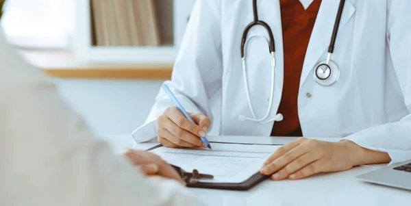 Mulher-médico desconhecida preenchendo um formulário de inscrição enquanto consulta o paciente. Conceito de medicina — Fotografia de Stock