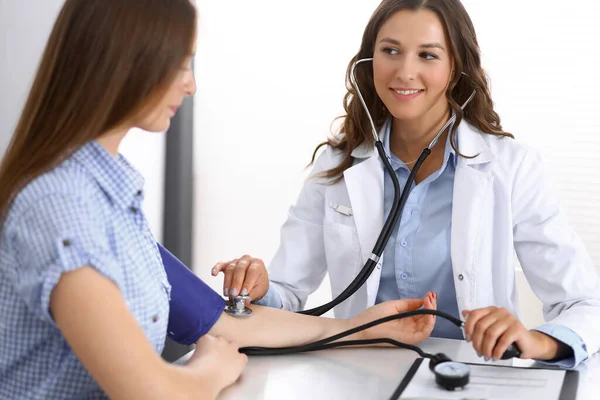 Läkaren kontrollerar blodtrycket hos kvinnliga patienter när de sitter vid skrivbordet på sjukhusets kontor. Kardiologi inom medicin och hälsovård — Stockfoto