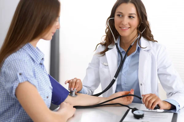 Doctor checking blood pressure of female patient while sitting at the desk in hospital office. Cardiology in medicine and health care concept Royalty Free Stock Photos