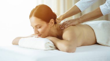 Güzel esmer kadın güneşli spa salonunda sırt masajından hoşlanıyor. Güzellik konsepti. Soğuk tonlu resim