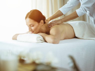 Güzel esmer kadın güneşli spa salonunda sırt masajından hoşlanıyor. Güzellik konsepti. Soğuk tonlu resim