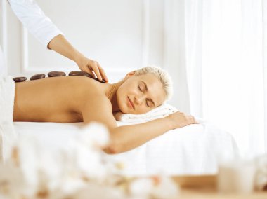 Güzel sarışın kadın sıcak taşlardan hoşlanıyor ve gözleri kapalı. Spa konsepti