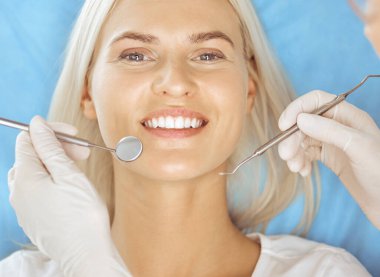 Diş hekiminde dişçi tarafından muayene edilen gülümseyen sarışın kadın. Sağlıklı diş ve ilaç konsepti