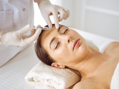 Güzellik uzmanı, genç esmer kadının yüzüne şırıngayla güzellik prosedürü uyguluyor. Kozmetik ilaç ve ameliyat, güzellik iğneleri.