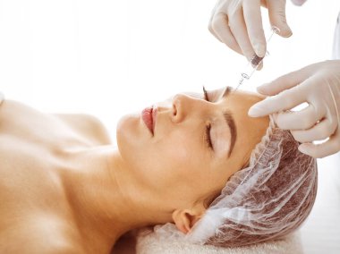 Güzellik uzmanı, genç esmer kadının yüzüne şırıngayla güzellik prosedürü uyguluyor. Kozmetik ilaç ve ameliyat, güzellik iğneleri.