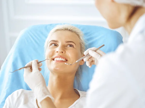 Lachende blonde vrouw onderzocht door tandarts in de tandheelkundige kliniek. Gezonde tanden en geneeskundeconcept — Stockfoto