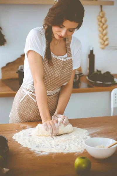 Jonge brunette vrouw koken pizza of handgemaakte pasta in de keuken. Huisvrouw maakt deeg op houten tafel. Dieet-, voedings- en gezondheidsconcept — Stockfoto