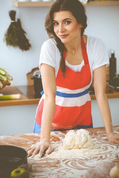 Jonge brunette vrouw koken pizza of handgemaakte pasta in de keuken. Huisvrouw maakt deeg op houten tafel. Dieet-, voedings- en gezondheidsconcept — Stockfoto