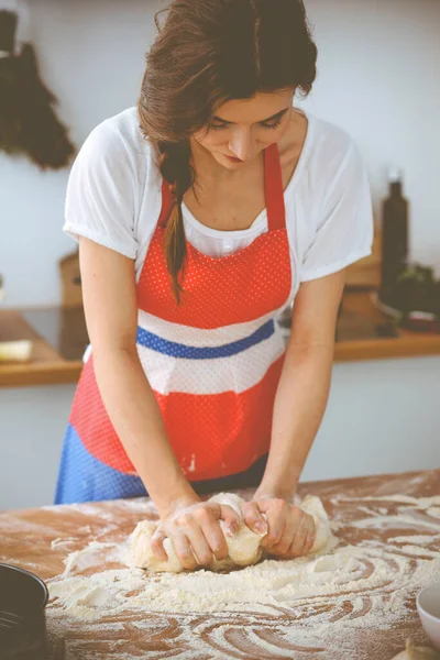 Jovem morena cozinhando pizza ou massa artesanal na cozinha. Dona de casa que prepara a massa de farinha na mesa de madeira. Conceito de alimentação, alimentação e saúde — Fotografia de Stock