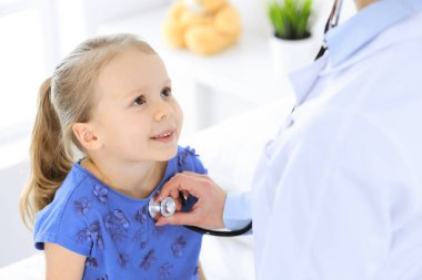 Doktor steteskopla küçük bir kızı muayene ediyor. Her zamanki tıbbi muayenede gülümseyen çocuk hasta. Tıp ve sağlık hizmetleri kavramları