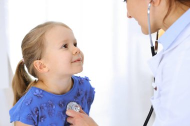 Doktor steteskopla küçük bir kızı muayene ediyor. Her zamanki tıbbi muayenede gülümseyen çocuk hasta. Tıp ve sağlık hizmetleri kavramları