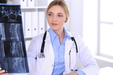 Doktor kadın hastanenin penceresinin yakınındaki röntgen filmini inceliyor. Cerrah ya da ortopedist. Tıp ve sağlık hizmetleri kavramı. Bir terapistin mavi renkli bluzu iyi görünüyor.