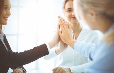 İş adamları takım çalışmasını göstermekten ve güneşli ofiste birlik ve ortaklık göstermekten mutlu olurlar. Başarı ve dostluk kavramları