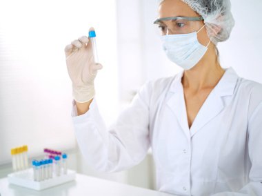 Koruyucu gözlüklü profesyonel kadın bilim adamı laboratuarda reaktörlerle araştırma tüpü kullanıyor. Tıp ve araştırma kavramları