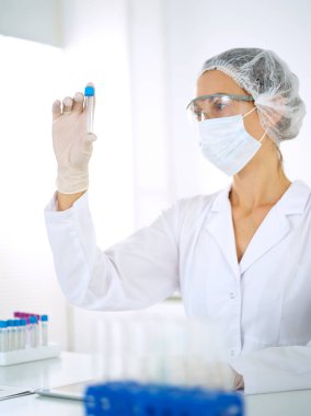 Koruyucu gözlüklü profesyonel kadın bilim adamı laboratuarda reaktörlerle araştırma tüpü kullanıyor. Tıp ve araştırma kavramları