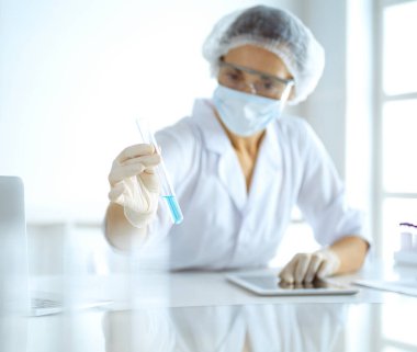 Koruyucu gözlüklü profesyonel kadın bilim adamı laboratuarda reaktörlerle araştırma tüpü kullanıyor. Tıp ve araştırma kavramları