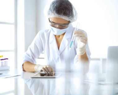 Koruyucu gözlüklü profesyonel kadın bilim adamı laboratuarda reaktörlerle araştırma tüpü kullanıyor. Tıp ve araştırma kavramları