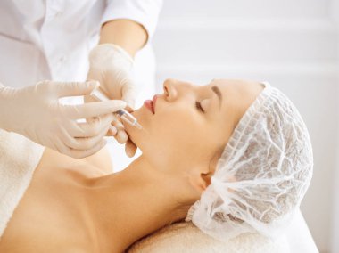 Güzel bir kadın kapalı gözlerle güzellik iğneleri yaptırıyor. Güzellik uzmanı elleri şırıngayla kadın yüzüne güzellik prosedürü uyguluyor. Kozmetik tıp ve cerrahi konsepti