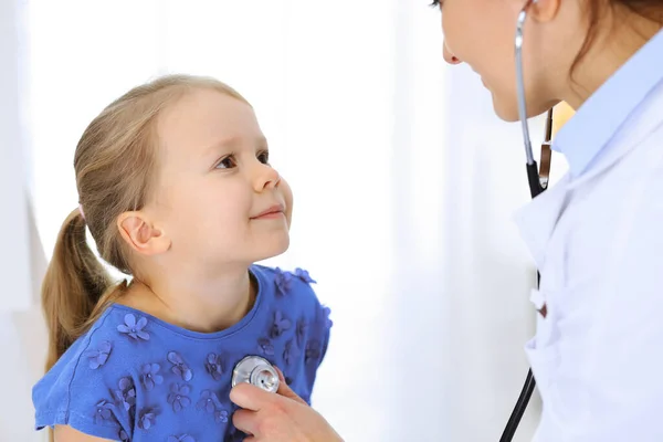 Arzt untersucht ein kleines Mädchen per Stethoskop. Glücklich lächelnder Kinderpatient bei der üblichen ärztlichen Untersuchung. Medizin- und Gesundheitskonzepte — Stockfoto