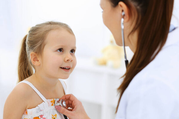 Доктор осматривает маленькую девочку стетоскопом. Счастливого улыбающегося ребенка при обычном медицинском осмотре. Медицина и здравоохранение