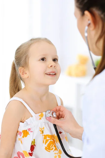 Doutor examinando uma menina por estetoscópio. Paciente de criança sorridente feliz em inspeção médica habitual. Conceitos de medicina e saúde — Fotografia de Stock