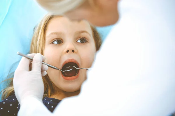 Liten flicka sitter vid tandstolen med öppen mun under oral kontroll medan läkare. Besökande tandläkarmottagning. Medicinskt koncept. Tonat foto — Stockfoto