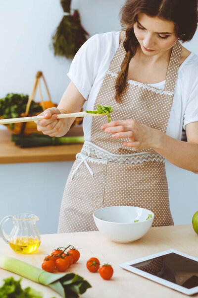 Молодая брюнетка готовит на кухне. Домохозяйка держит в руке деревянную ложку. Концепция питания и здоровья