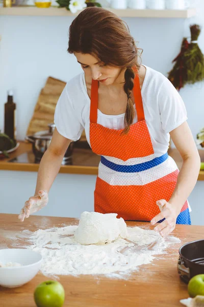 Jovem morena cozinhando pizza ou massa artesanal na cozinha. Dona de casa que prepara a massa de farinha na mesa de madeira. Conceito de alimentação, alimentação e saúde — Fotografia de Stock