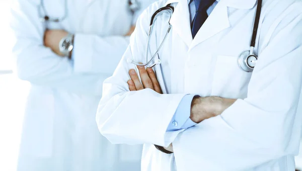 Doctor man standing straight and crossed arms with colleague at background, close-up. Group of doctors. Perfect medical service in clinic. Medicine and healthcare concepts. Toned picture