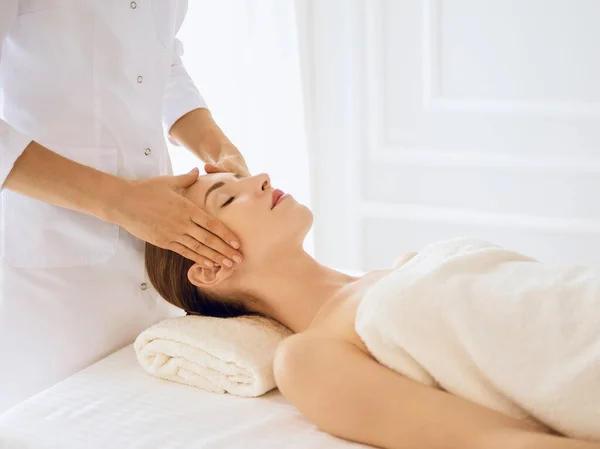 Hermosa mujer disfrutando de masaje facial con los ojos cerrados en el centro de spa. Concepto de tratamiento relajante en medicina —  Fotos de Stock