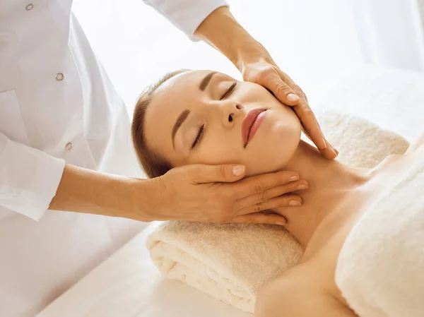 Hermosa mujer disfrutando de masaje facial con los ojos cerrados en el centro de spa. Concepto de tratamiento relajante en medicina — Foto de Stock