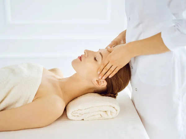 Piękna kobieta korzystająca z masażu twarzy z zamkniętymi oczami w centrum spa. Relaksująca koncepcja leczenia w medycynie — Zdjęcie stockowe
