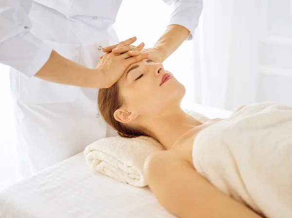 Красива жінка насолоджується масажем обличчя з закритими очима в спа-центрі. Розслаблююча концепція лікування в медицині — стокове фото