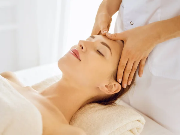 Hermosa mujer disfrutando de masaje facial con los ojos cerrados en el centro de spa. Concepto de tratamiento relajante en medicina — Foto de Stock