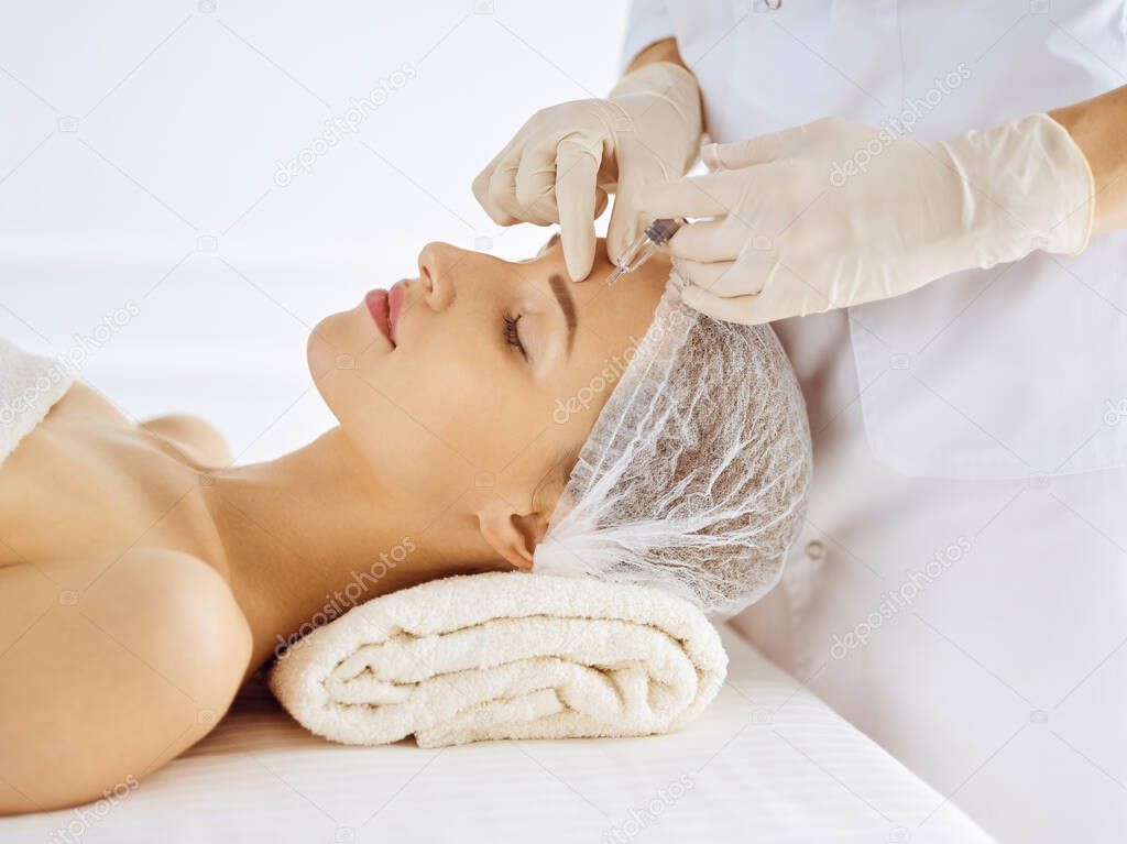 Beautiful woman receiving beauty injections with closed eyes. Beautician doctor hands doing beauty procedure to female face with syringe. Cosmetic medicine and surgery concept