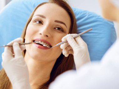 Diş hekiminde dişçi tarafından incelenen diş telleriyle gülümseyen genç bir kadın. Sağlıklı diş ve ilaç konsepti