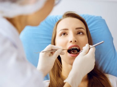 Diş hekiminde dişçi tarafından incelenen diş telleriyle gülümseyen genç bir kadın. Sağlıklı diş ve ilaç konsepti