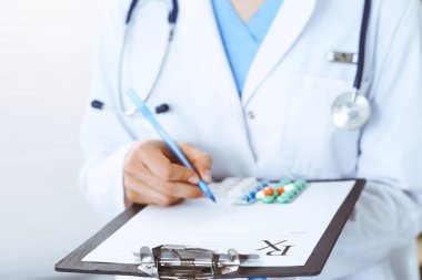 Hastanedeki kimliği belirsiz kadın doktor. Tıbbi panodaki haplar. Genç kadın doktor hastane ofisinde otururken reçete yazıyor ya da form dolduruyor.