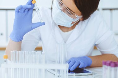 Koruyucu gözlüklü profesyonel kadın bilim adamının laboratuarda reaktörlerle deney yapması. Tıp ve araştırma konsepti