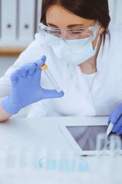 Koruyucu gözlüklü profesyonel kadın bilim adamının laboratuarda reaktörlerle deney yapması. Tıp ve araştırma konsepti