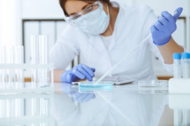 Koruyucu gözlüklü profesyonel kadın bilim adamının laboratuarda reaktörlerle deney yapması. Tıp ve araştırma konsepti