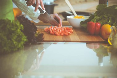 Mutfakta pişen bilinmeyen insan elleri. Kırmızı domatesleri dilimleyen kadın. Sağlıklı yemek ve vejetaryen gıda konsepti.