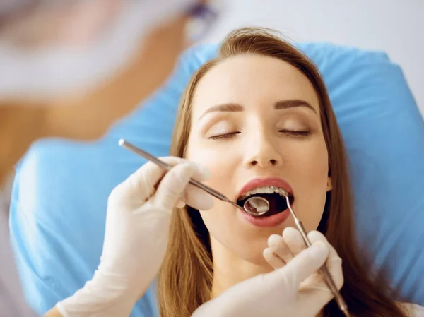 Uśmiechnięta młoda kobieta z nawiasami ortodontycznymi badana przez dentystę w klinice dentystycznej. Zdrowe zęby i koncepcja medycyny — Zdjęcie stockowe