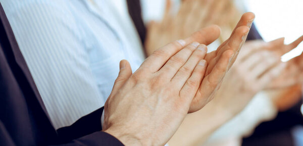 Деловые люди хлопают и аплодируют на митинге или конференции, крупным планом рук. Группа неизвестных бизнесменов и женщин в современном белом офисе. Концепция командной работы или корпоративного тренерства