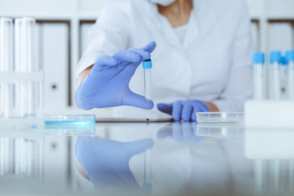 Close-up of professional female scientist in protective eyeglasses making experiment with reagents in laboratory. Medicine and research concept