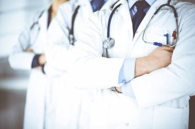 Hastane ofisinde çapraz kolları ve steteskopları olan bir grup modern doktor bir takım gibi duruyor. Doktorlar hastaları muayene etmeye ve yardım etmeye hazır. Tıbbi yardım, sağlık sigortası, en iyi hastalık tedavisi ve ilaç konsepti.