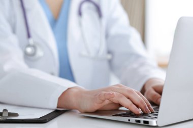Masada otururken dizüstü bilgisayarda yazan kimliği belirsiz kadın doktor. Tıp konsepti.