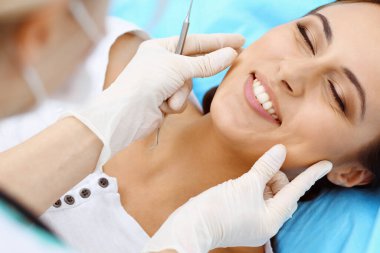 Genç bayan hasta dişçi muayenehanesini ziyaret ediyor. Sağlıklı, beyaz dişleri olan güzel bir kadın diş hekimliğinde çalışırken ağız muayenesi sırasında diş sandalyesinde oturuyor. Diş sağlığı kliniği, stomatoloji konsepti