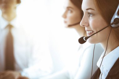 Çağrı merkezi ve iş adamları konsepti. Kulaklıklı, müşterilere danışan güzel bir iş kadını. Ofiste çalışan çeşitli telefon operatörleri.